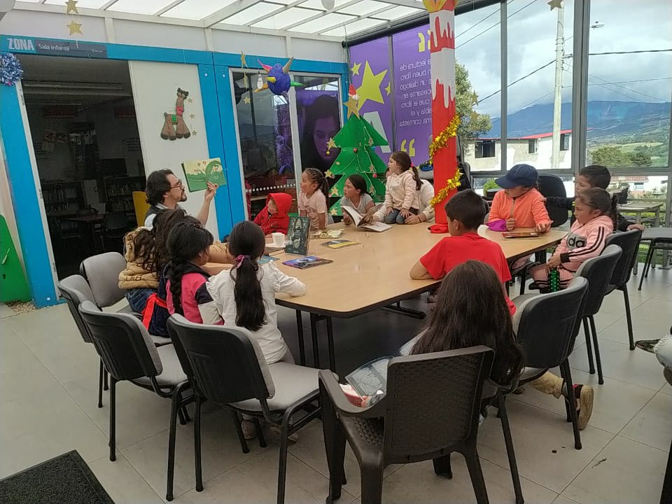 niños y niñas observando un libro ilustrado mientras el profesor lo lee en voz alta.