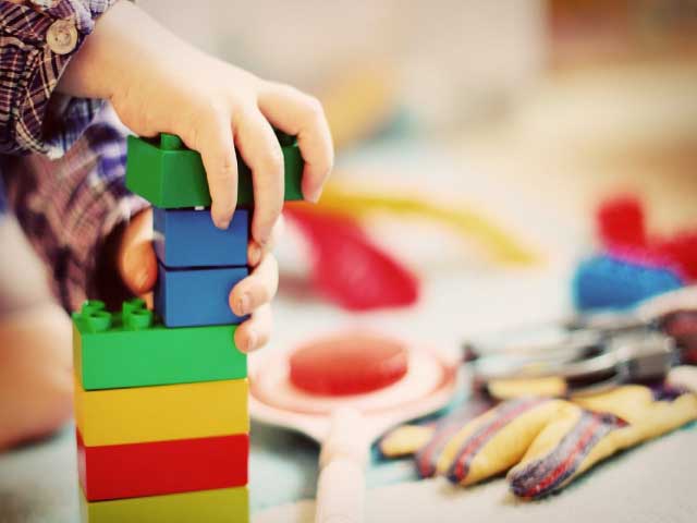 manos de un niño pequeño jugando y apilando piezas de colores.