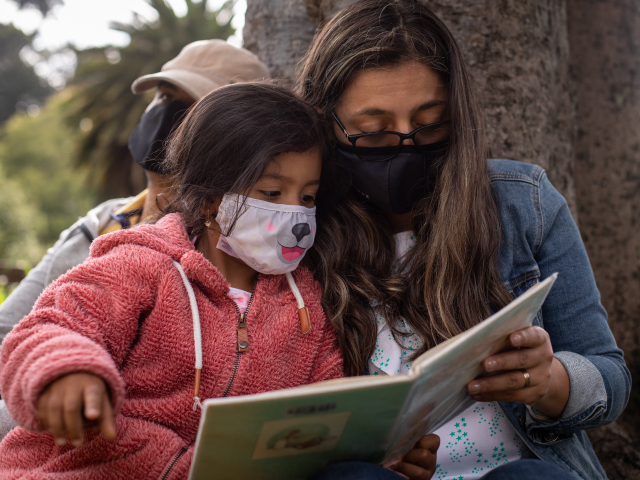 Niña y acompañante comparten lectura al aire libre