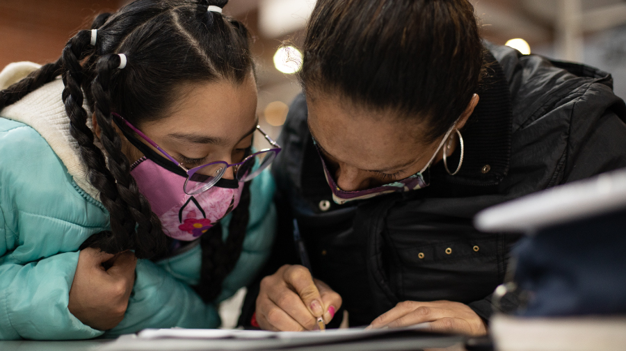 niña y mujer realizando un ejercicio de escritura sobre papel en biblioteca pública