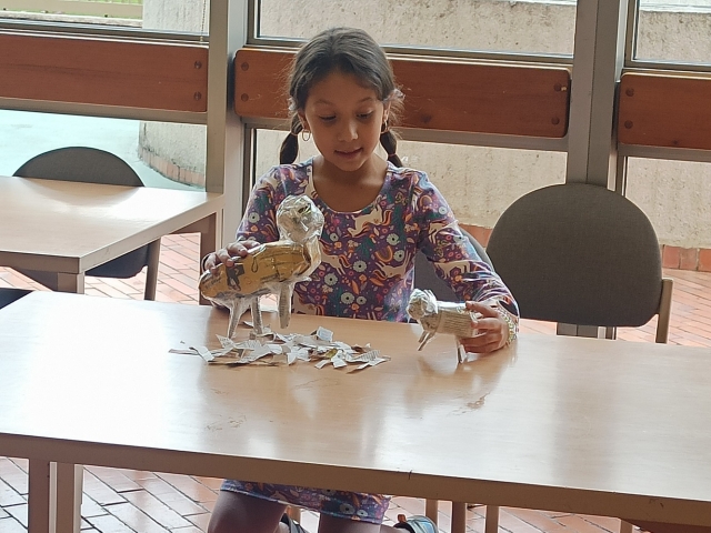 niña jugando con animales hechos de papel periódico sobre un escritorio de madera.