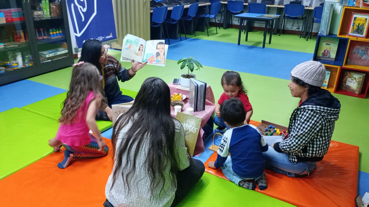 Niños y adultos disfrutan de libros y juegos en una sala de lectura colorida. 