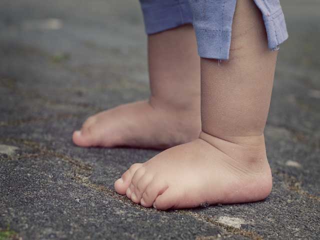 pies descalzos de un bebé parado sobre el suelo color gris.