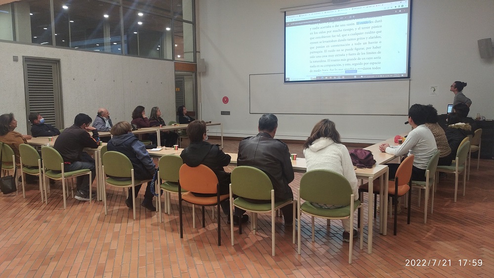 un grupo de adultos sentados en mesa redonda al frente de la proyección de una pantalla que muestra una parte del texto que están hablando. 