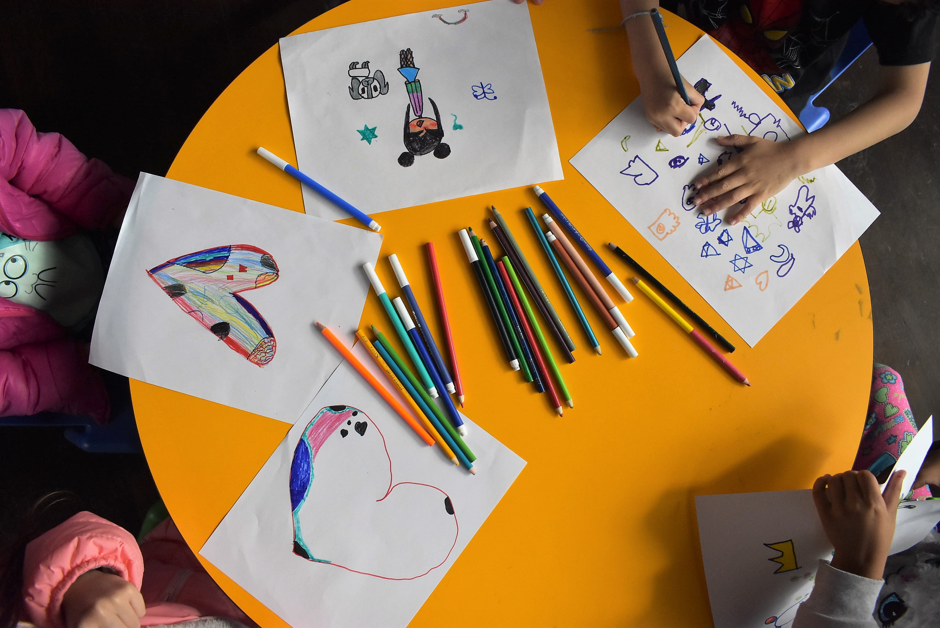 niños y niñas dibujando con lapices de colores sobre una mesa color amarilla.