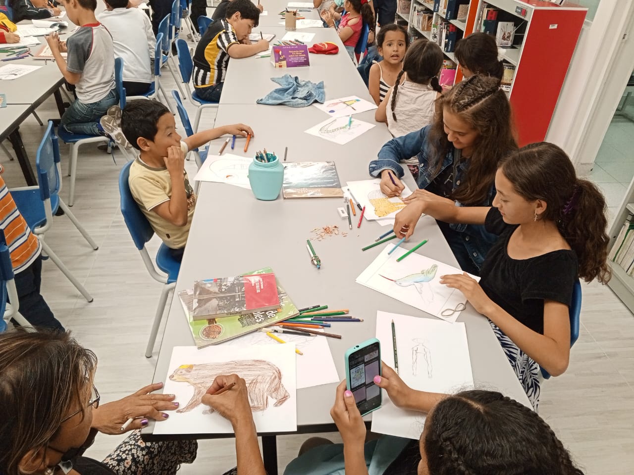 niños y niñas de diferentes edades dibujando con lapices de colores sobre una mesa blanca.