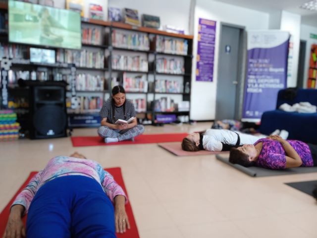 mujeres jóvenes en una clase de yoga y relajación acompañadas de la instructora mientras les lee un libro en voz alta.