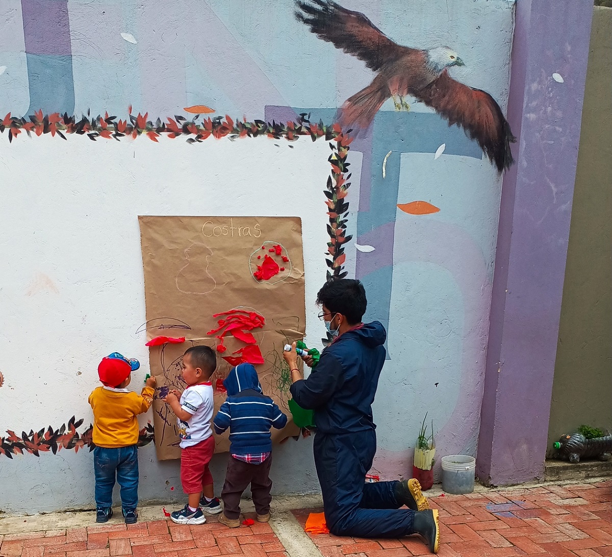 niños pequeños dibujando sobre un pliego de papel pegado en una pared