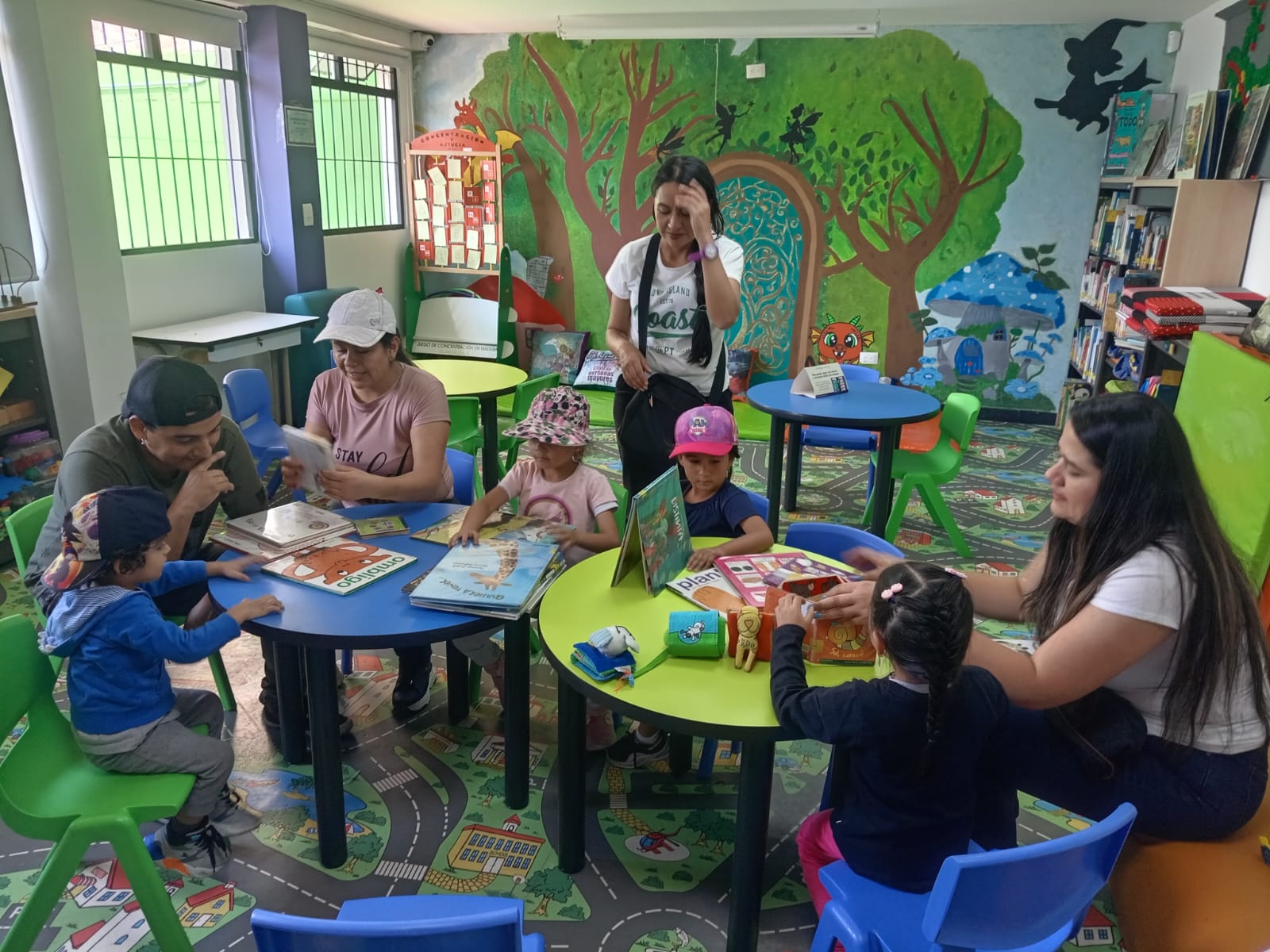 niños y niñas acompañados de sus cuidadores y una docente mientras leen un libro en voz alta 