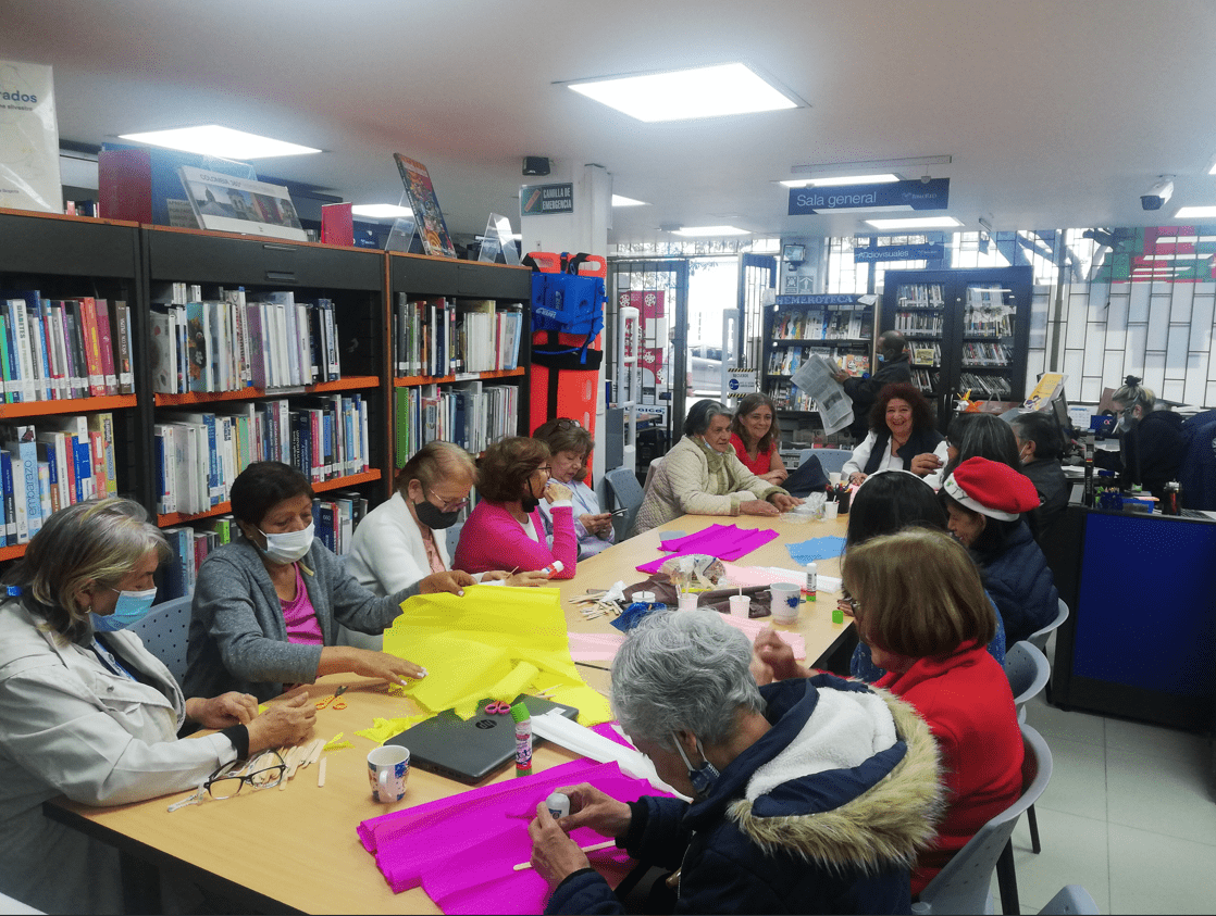 Grupo de personas mayores en medio de un taller de manualidades cortando papel de colores
