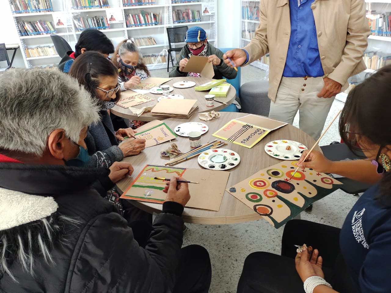 grupo de adultos mayores pintando en medio de un taller de manualidades.